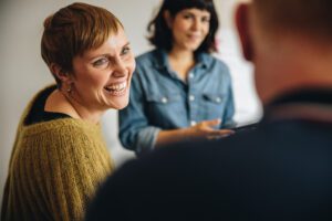Woman smiling while participating in an Intensive Outpatient Program (IOP) group therapy session, engaging with peers in a supportive setting.