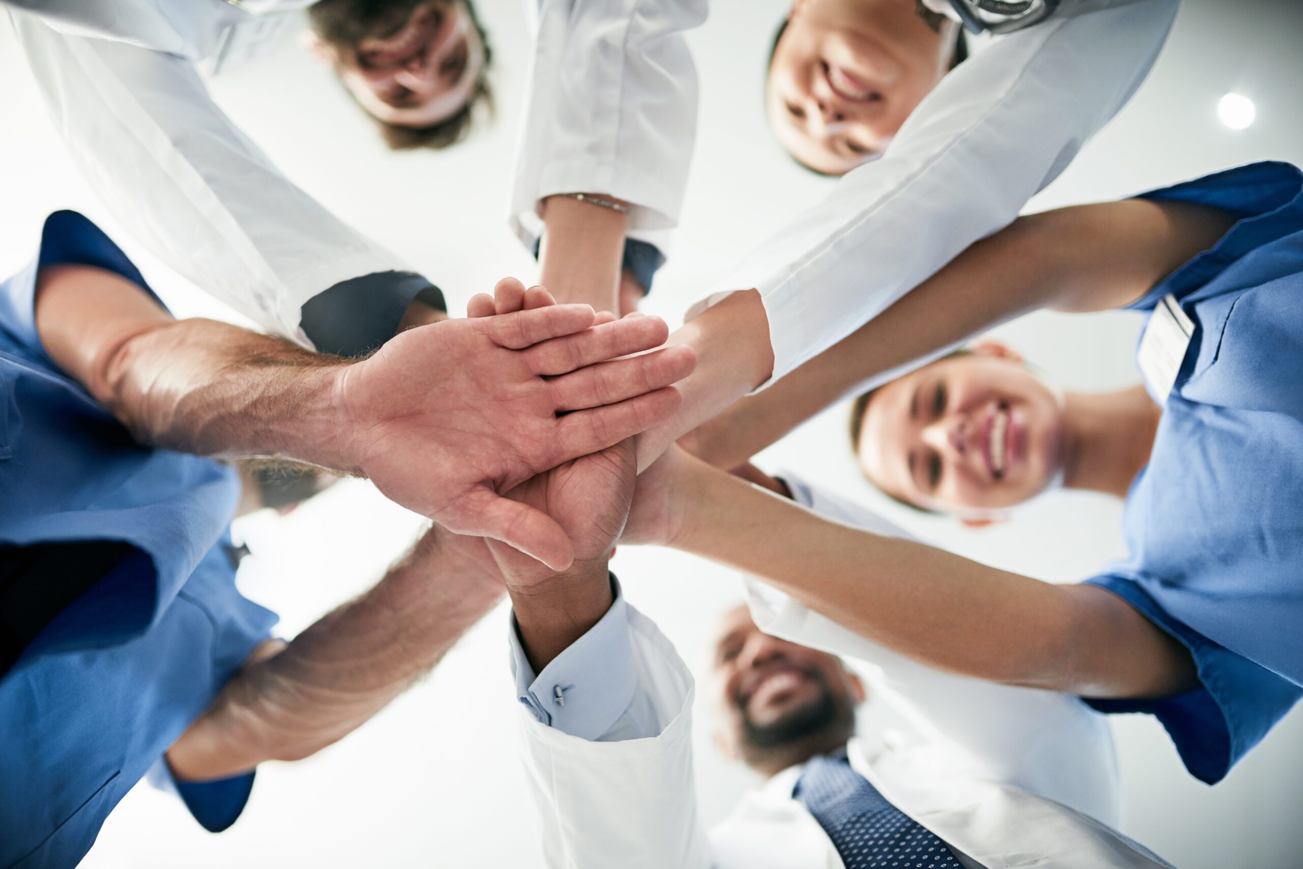 Team of medical and behavioral health professionals standing in a circle with hands together, symbolizing unity and teamwork in healthcare.