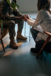 A psychotherapist is in a session with a soldier with mental health issues and holding his hands in support.