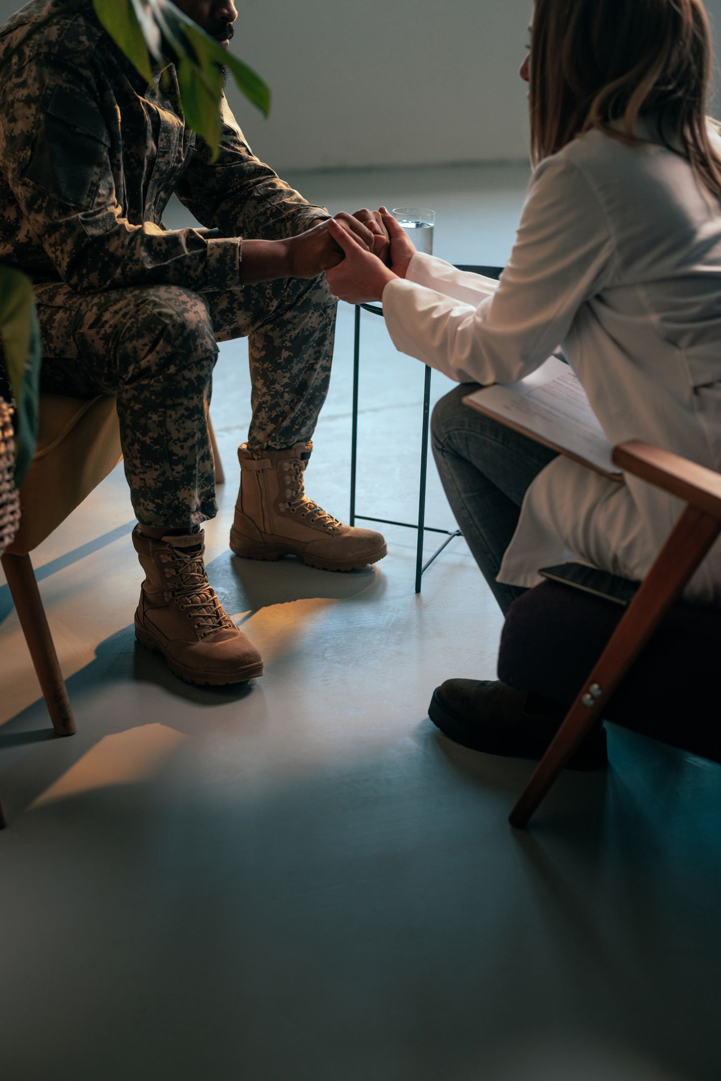 A psychotherapist is in a session with a soldier with mental health issues and holding his hands in support.
