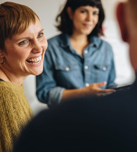 Careers Woman smiling while participating in an Intensive Outpatient Program (IOP) group therapy session, engaging with peers in a supportive setting.